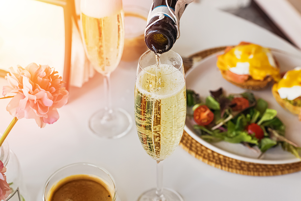 Pouring prosecco sparkling wine in a glass on sunday brunch with blurred eggs royal on the background.